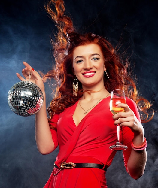 Belle femme rousse sexy avec un verre de vin blanc et une boule disco