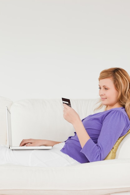 Belle femme rousse en utilisant un ordinateur portable et un téléphone en position couchée sur un canapé