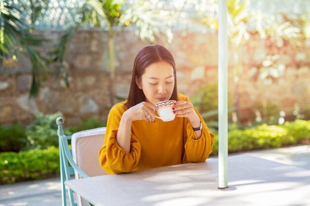 Belle femme s&#39;asseoir sur la table en buvant un café au café en plein air dans le jardin.