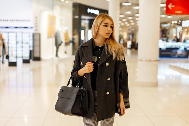 Belle femme avec un sac de mode dans un manteau élégant à la mode dans le centre commercial