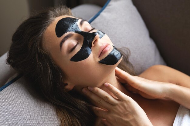 Une belle femme se détend à la maison avec un masque détachable noir sur le visage.