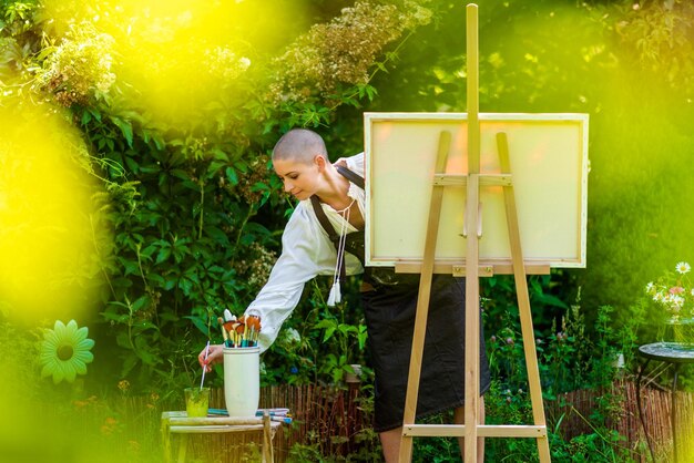 Photo une belle femme se détend en peignant une toile d'art à l'extérieur dans son concept de créativité de jardin