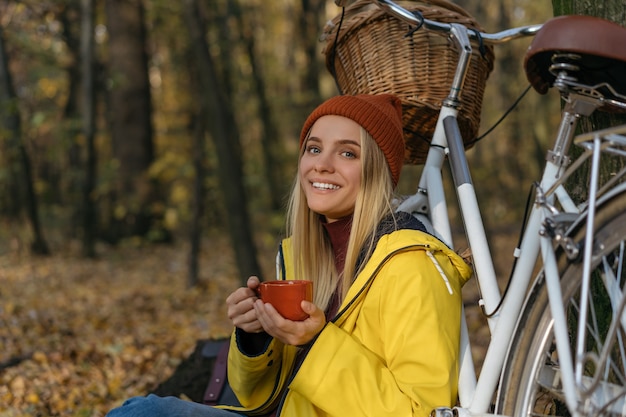 Belle femme se détendre dans la forêt d'automne, tenant une tasse de café, à la recherche