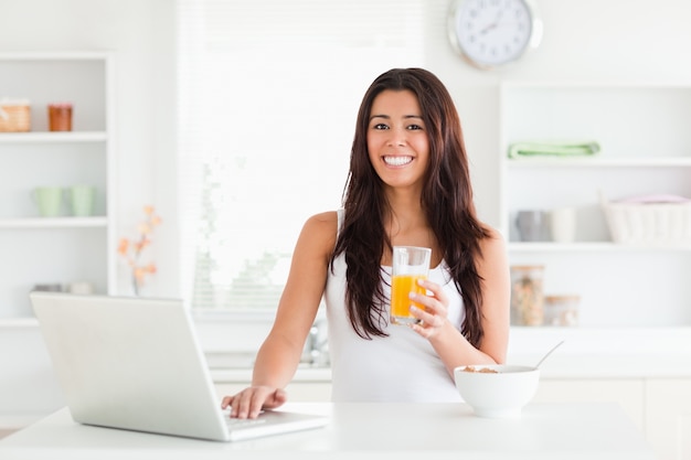 Belle femme se détendre avec son ordinateur portable tout en tenant un verre de jus d&#39;orange