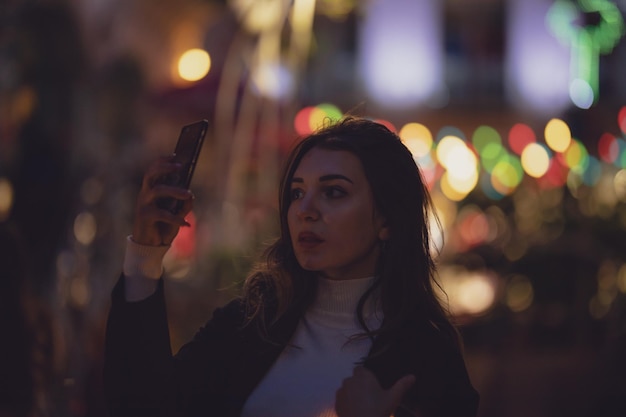 Une belle femme se fait un selfie dans une ville éclairée la nuit.