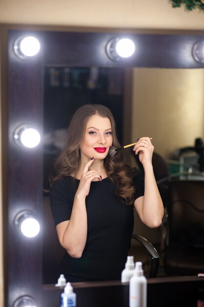 Belle femme se maquille et se regarde dans le miroir