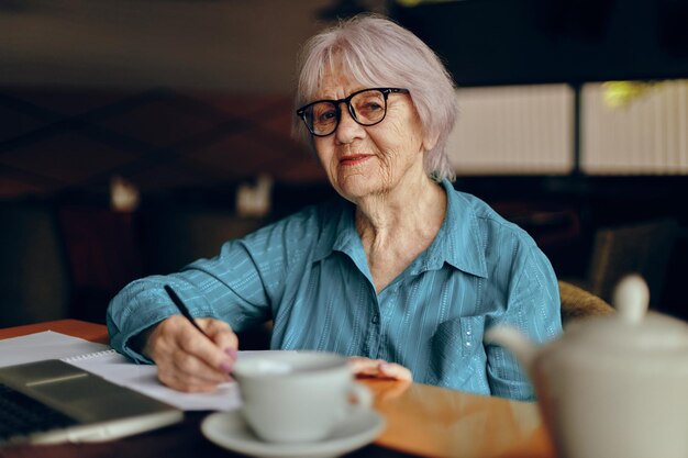 Belle femme senior mature avec des lunettes est assise à une table devant un ordinateur portable inchangé