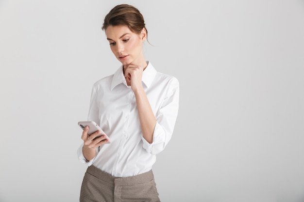 Belle femme sérieuse tapant sur téléphone mobile isolé sur fond blanc