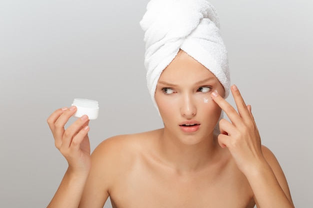 Belle femme avec une serviette blanche et un pot de crème