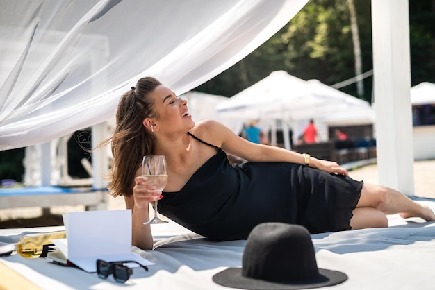 Belle femme sexy insouciante allongée sur un belvédère avec un rideau blanc sur la plage