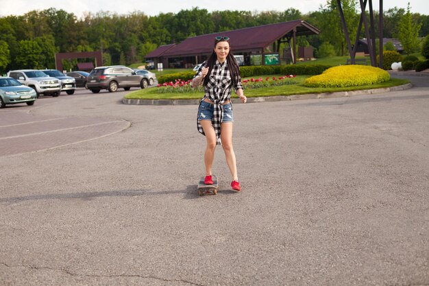 Belle femme en slip patine sur l'asphalte en chaussures roses sur fond de voitures.