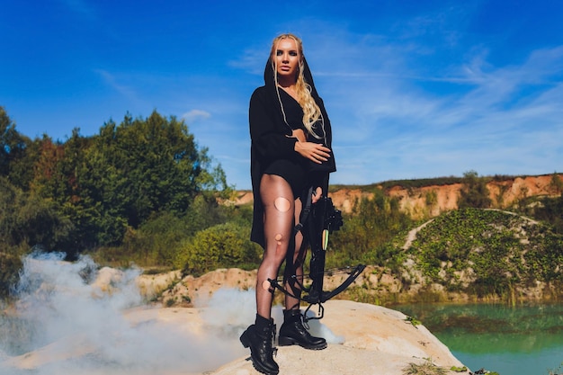 Belle femme soldat tenant un fusil debout sur un rocher sur le soleil brûlant du ciel bleu de la montagne