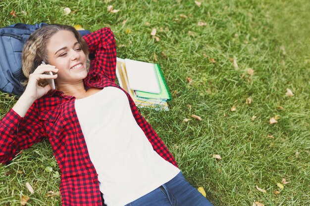 Belle femme souriante allongée sur l'herbe et parlant sur mobile. Technologie, médias sociaux, éducation et concept indépendant, espace de copie