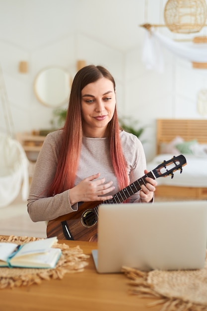 Une belle femme souriante apprend à jouer du ukulélé à distance. L'enseignant donne une leçon de ukulélé en ligne.