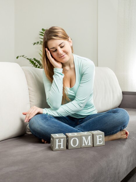 Belle femme souriante assise sur un canapé et regardant le mot "maison"