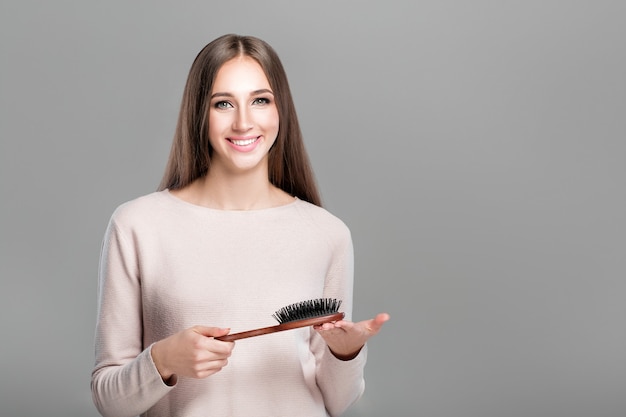 Belle femme souriante aux longs cheveux naturels lisses tient la brosse à cheveux