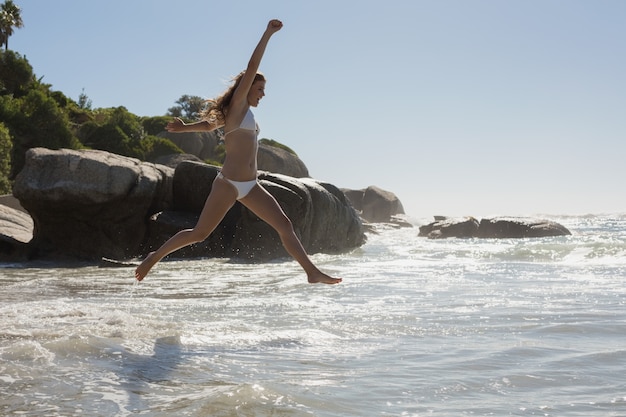 Belle femme souriante en bikini blanc, sautant sur la plage