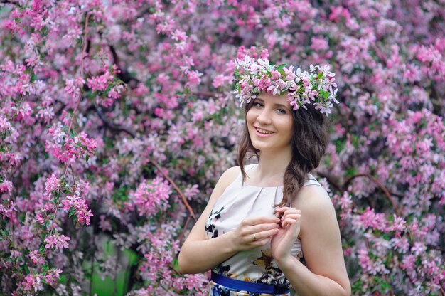 Belle femme souriante avec une couronne dans le jardin printanier en fleurs