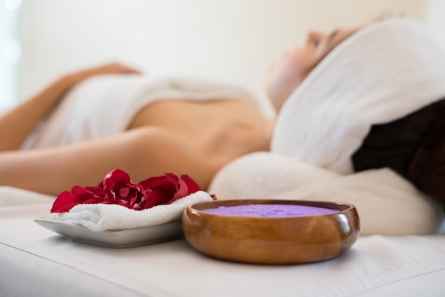 Belle femme souriante avec des fleurs se reposant dans le spa avant le massage.