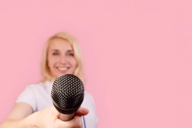 Une belle femme souriante sur fond rose avec un microphone Émotions positives