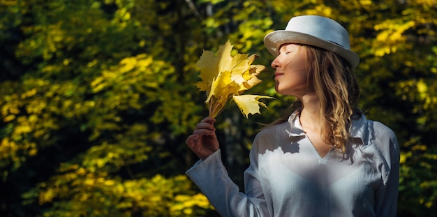 Belle femme souriante heureuse a tenu un bouquet de feuilles d'érable jaune sur son visage