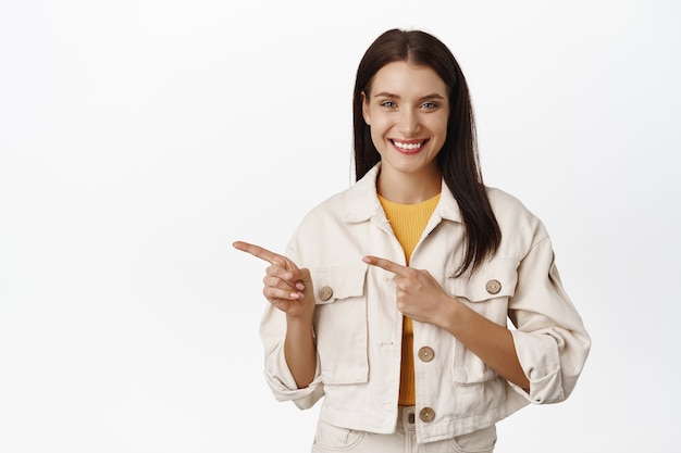 belle femme souriante pointant vers la gauche, montrant une bannière de vente ou de publicité, l'air heureuse, recommandant une entreprise ou un lieu, debout sur blanc.