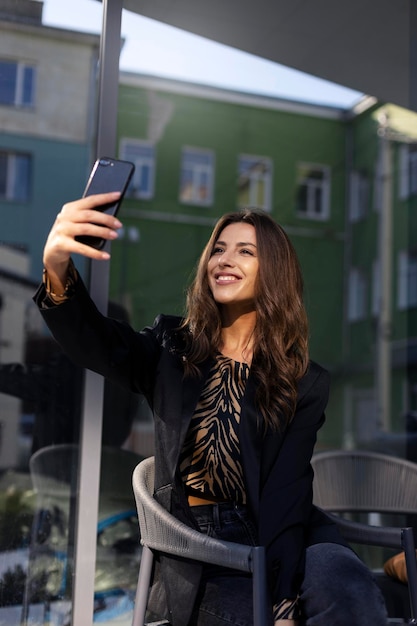 Belle femme souriante prend un selfie au téléphone Une fille joyeuse est assise tient un téléphone dans sa main et tire du contenu pour ses abonnés