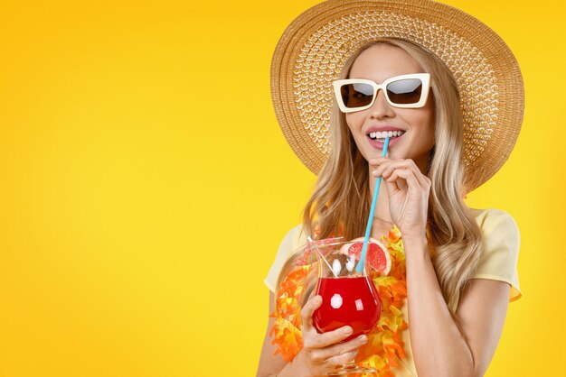 Belle femme souriante en robe d'été avec cocktail isolé sur fond jaune