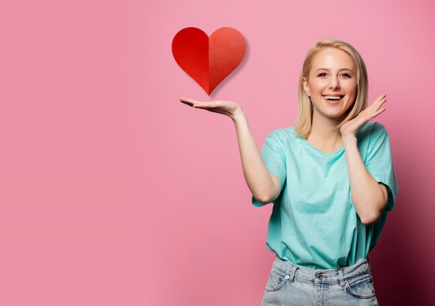 Belle femme souriante avec signe de forme de coeur sur mur rose