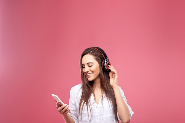 Belle femme souriante avec un smartphone dans les mains en écoutant sa musique préférée via un casque sans fil