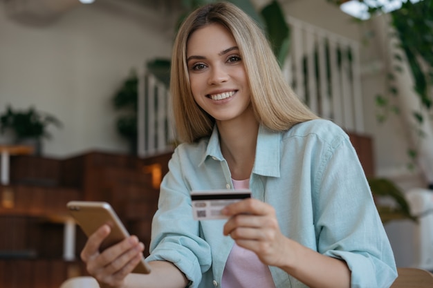 Belle femme souriante tenant une carte de crédit, à l'aide de smartphone pour les achats en ligne.