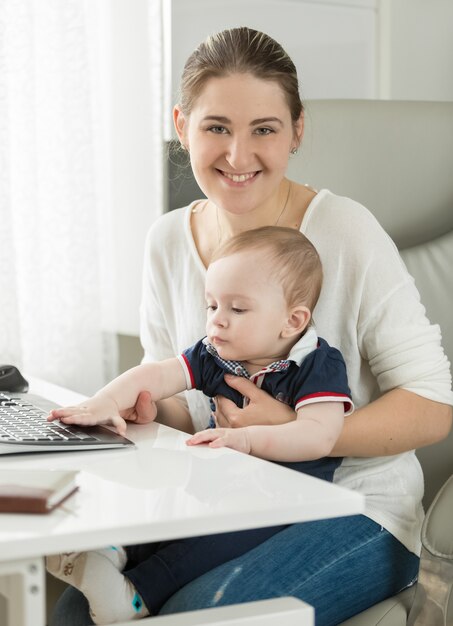 Belle femme souriante travaillant sur ordinateur avec son bébé