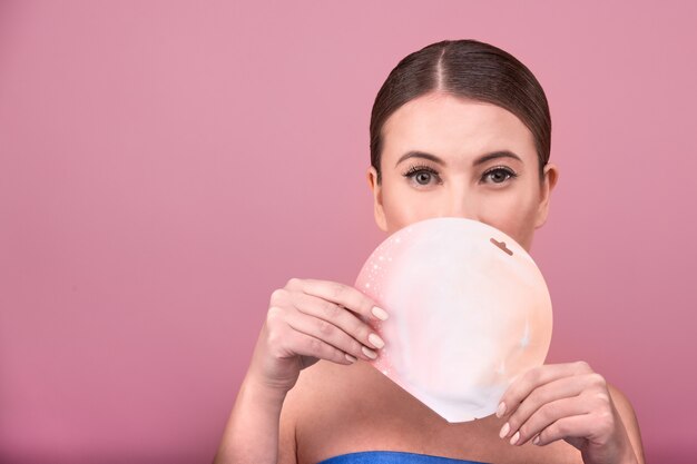 Belle femme avec un sourire adorable tient dans son paquet de mains avec masque facial