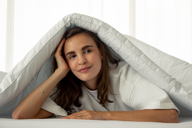 Belle femme sous une couverture blanche sur le lit.