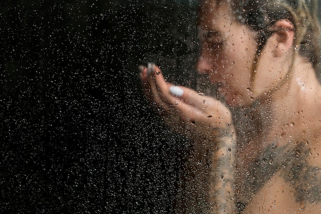 Belle femme sous la douche se lavant le visage, sur un fond sombre