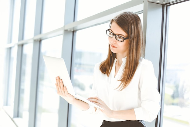 Belle femme spécialiste avec ordinateur portable debout dans un bureau moderne et souriant avec charme Travailler sur la stratégie de plan d'analyse des données de conception Concept de gens d'affaires