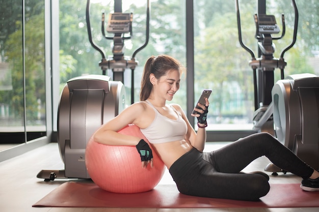 Belle femme de sport asiatique joue au téléphone intelligent dans la salle de gym