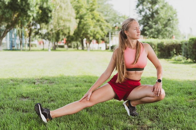 Belle femme sportive aux cheveux longs faisant des étirements dans le parc avant de faire du jogging