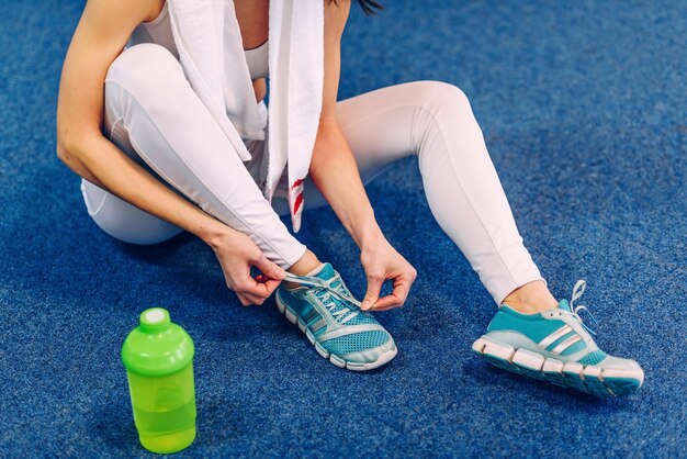 Belle femme sportive avec un corps parfait attachant des lacets sur des baskets dans la salle de gym