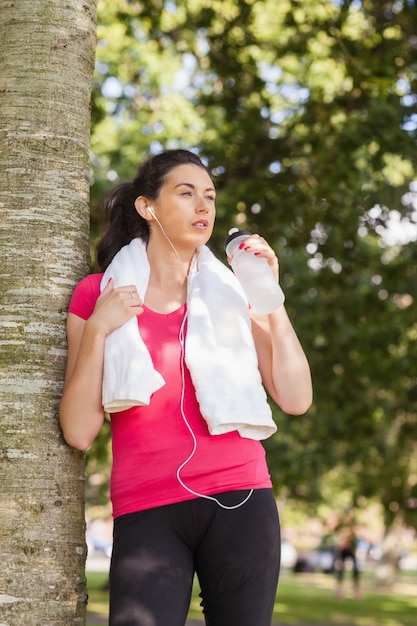 Belle femme sportive l&#39;eau potable et appuyé contre un arbre