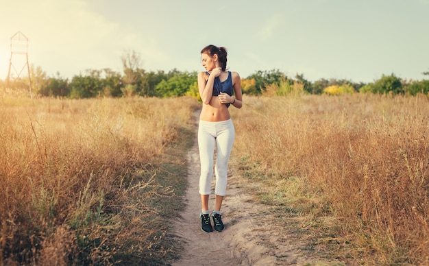 Belle femme sportive mince debout au coucher du soleil sur le terrain à l'automne.