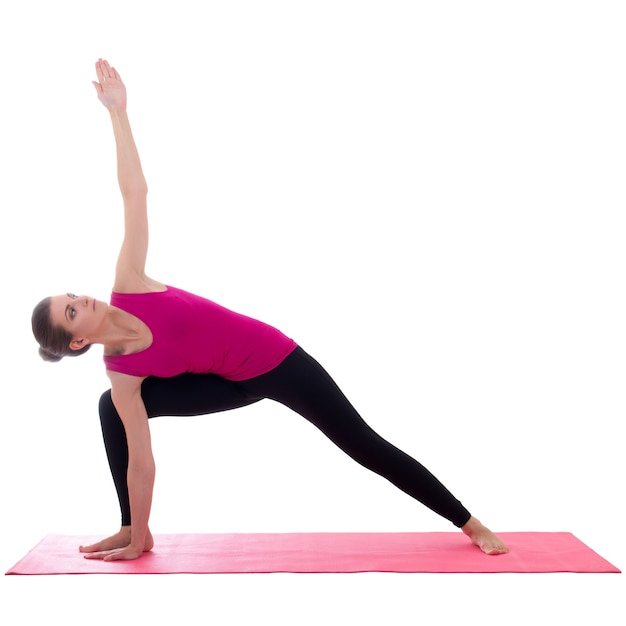 Belle femme sportive mince debout sur un tapis rose en pose de yoga isolé sur fond blanc