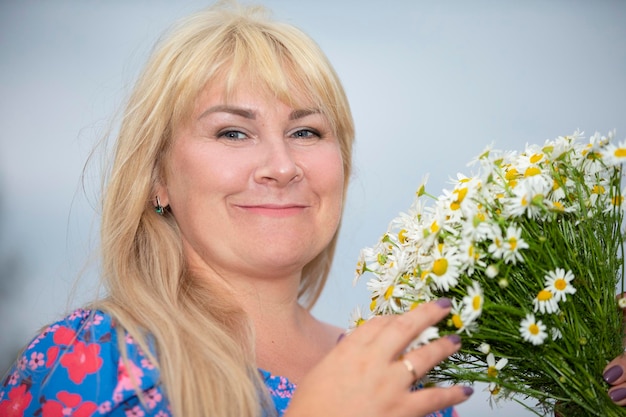 Une belle femme de taille plus aux cheveux blancs tient un bouquet de marguerites sourit profite de l'été et de la vie