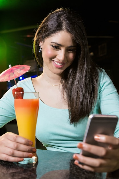 Belle femme tapant un message texte tout en ayant un cocktail au comptoir