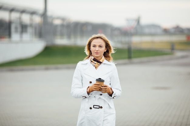 Belle femme avec une tasse de café près de l'immeuble de bureaux.