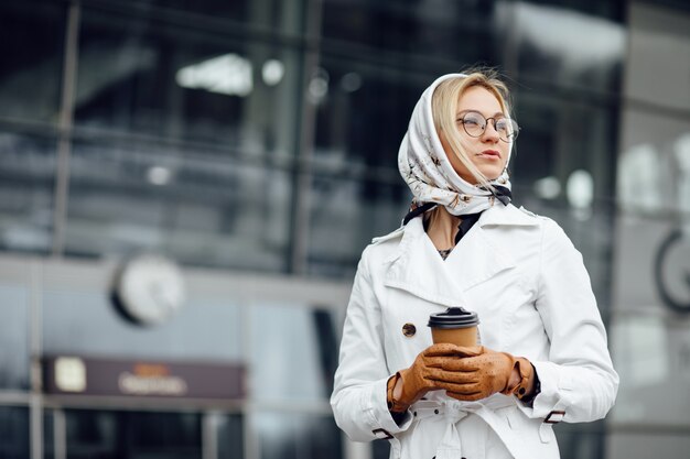 Belle femme avec une tasse de café près de l'immeuble de bureaux.