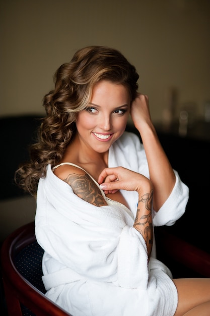 Belle femme avec un tatouage dans un manteau blanc sourit à l'hôtel.