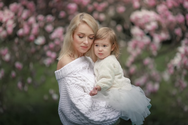 Belle femme tenant un bébé sur fond d'arbre fleuri avec des fleurs rouges