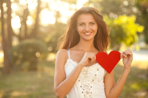 Belle femme tenant un coeur rouge derrière le dos