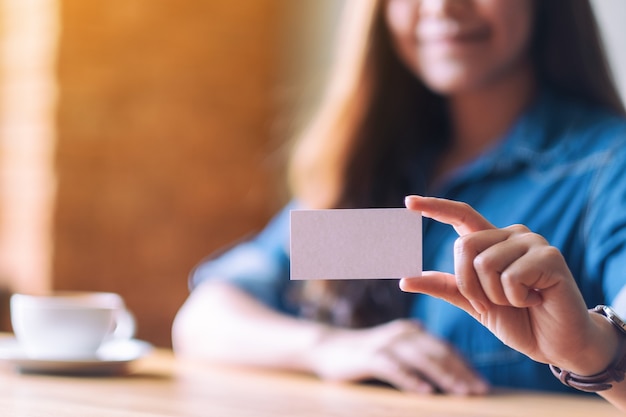 Une belle femme tenant et montrant une carte de visite vide vierge à quelqu'un